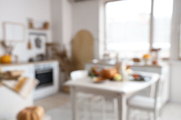 Blurred view of light kitchen with autumn decor, counters and dining table