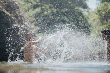 Two children joyfully splash water in a sunlit forest stream, capturing the essence of summer fun...