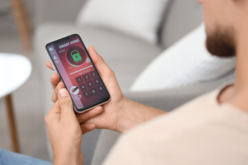 Young man using mobile phone with smart home security system application in room, closeup