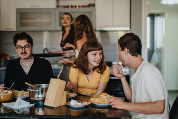 A group of young adults share a hearty meal and laughter in a contemporary kitchen setting,...