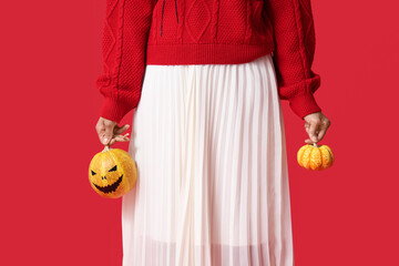 Beautiful young happy African-American woman with Halloween pumpkins on red background, closeup