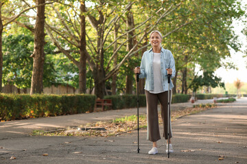 Beautiful mature happy woman training with walking poles in park