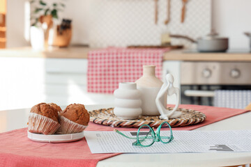 Eyeglasses with newspaper and muffins on dining table in kitchen, closeup