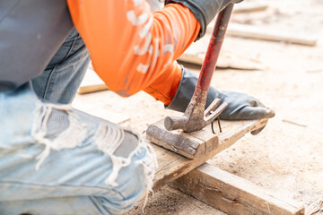 Worker pulling rusty nail out of old pinewood with hammer.