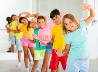 Group of cheerful tween children standing in row one by one, learning movements of vigorous funny...