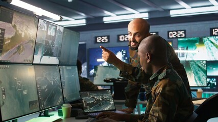 Army colleagues looking at screens in command center housing operational missile defense system designed to intercept ballistic rockets. Experts using tracking gear and radar systems, camera B