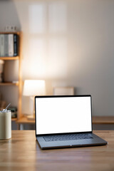 Mockup blank white screen laptop computer on wooden table in home office room.