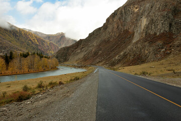 A two-lane asphalt road descends into the autumn valley along a high mountain and the banks of a...
