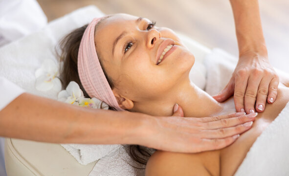 Young woman enjoying professional deep tissue massage of neck, collarbone and chest muscles to relieve tension and improve lymphatic drainage..