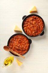 Pans with Bolognese sauce, oil and pieces of cheese on white wooden background, top view