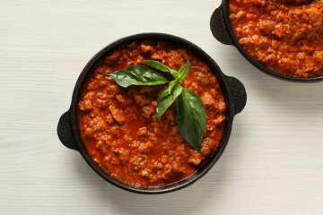 Pans with Bolognese sauce and basil on white wooden background, top view