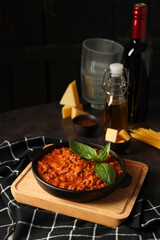 Bolognese sauce, glasses, bottle of wine and pieces of cheese on dark background