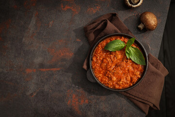 Bolognese sauce in frying pan, mushrooms and towel on dark background, space for text