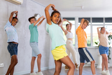 Dynamic little girl training Hip hop dance poses in dancehall with other attendees of dancing...