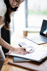 Cheerful business Asian woman freelancer making telephone call share good news about project working in office workplace, business finance concept.