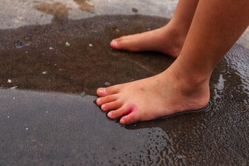 Toddler's feet stepped in puddles of rainwater on the asphalt road.
