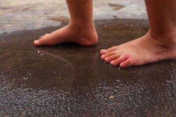 Toddler's feet stepped in puddles of rainwater on the asphalt road.
