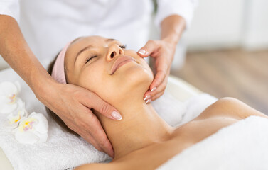Girl enjoys and rests during massage face skin procedure in beauty salon, professional woman performs relaxing stroking and patting while working out problem areas of neck.