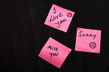 Pink Paper Notes with Handwritten 'I Love You', 'Miss You', and 'Sorry' on Black Background