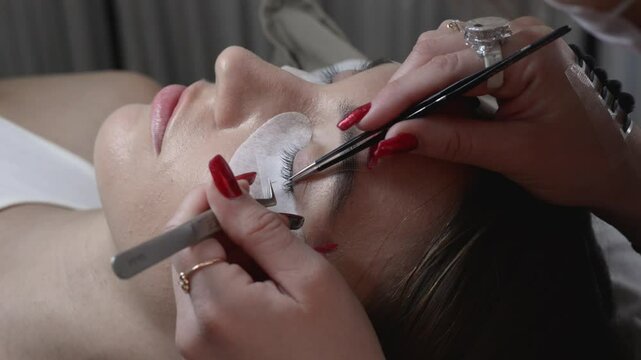Close up of beauty model's face during procedures of eye lash extension and master's hand with tweezers
