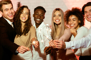 New Year Concept. Cheerful Millennials Holding Burning Sparklers Having Party Standing Indoor.