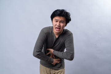 An Asian man grimacing in pain, clutching his stomach with both hands, suggesting abdominal...