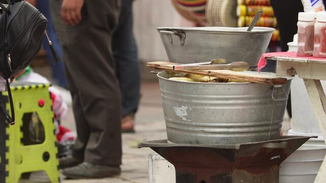mexican street food, a big container full with elotes are cooking on coal, elotes, mexican sweet corn street vendor, informal work, boling sweet corn