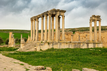 Fototapeta premium Scenic view of Temple of Juno Caelestis, well-preserved Roman ruins in Dougga, surrounded by spring greenery in Tunisia, against cloudy backdrop