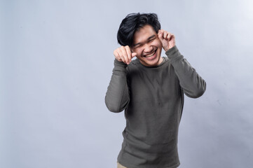 An Asian man playfully mimicking a cat's paw gesture with both hands near his face while smiling....