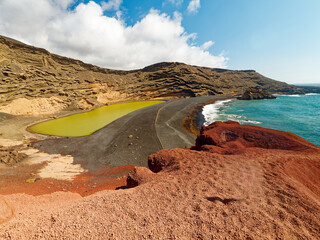 breathtaking aerial view of Charco de los Clicos on Lanzarote. The emerald green lagoon is nestled amidst a colorful volcanic landscape of red cliffs, black sand beaches, and yellow volcanic rocks. 
