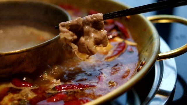 using chopsticks in spicy hot pot with sliced beef mutton lamb meat