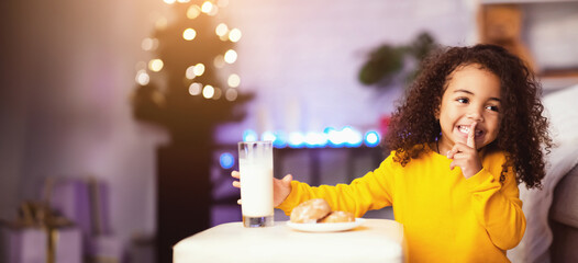 Shhh, it's secret. Adorable girl preparing milk and cookies for Santa Claus, free space
