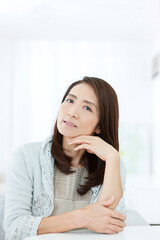 椅子に座って考え事をするシニア女性