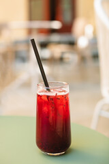 A glass of berry lemonade drink on a cafe table outdoors in summer.