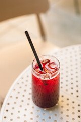 Iced fruit lemonade drink in a clear glass on a cafe table outdoors in summer.