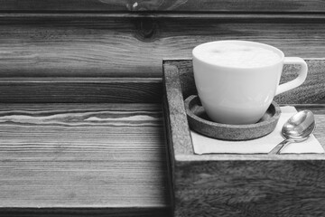 White coffee cup with spoon on wooden tray, black and white. Americano with milk on serving tray, monochrome. Coffee break concept. Served hot drink in restaurant. Coffee table close up. Hot drinks.