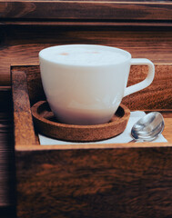 White coffee cup with spoon on wooden tray. Americano with milk on serving tray. Coffee break concept. Served hot drink in restaurant. Coffee table close up. Hot drinks concept. 