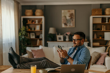 A smiling male freelancer with eyeglasses using a laptop while working from home