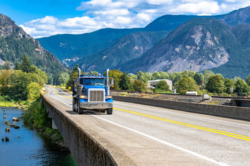 Blue tipper big rig semi truck with tip trailer running on the transportation bridge across the...