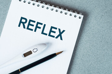 White Notebook With The Word Reflex Written In Blue Ink On A Gray Surface
