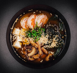 Steaming bowl of miso soup with tofu, shrimp, and mushrooms