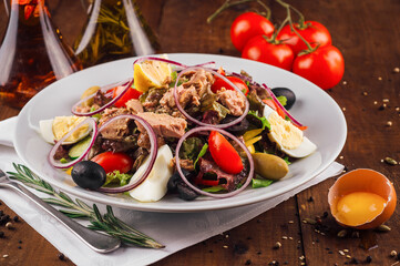 Fresh nicoise salad with tuna on a wooden table being prepared with eggs and tomatoes around