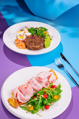 Two healthy dishes with quinoa, smoked salmon, omelette and ham served on white plates