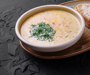 Creamy fish soup served in bowl with bread and grilled lemon on dark background