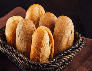 Freshly baked bread rolls lying in wicker basket on brown napkin