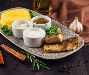 Fried fish fillet served on plate with polenta and sauces