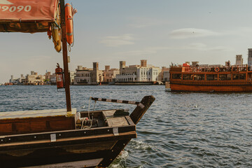 Dubai, UAE - January 6, 2020: Wooden dhow boat docked at Dubai Creek with Al Fahidi historical buildings in the background