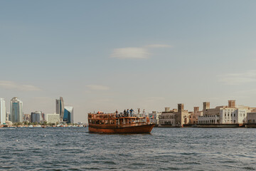 Dubai, UAE - January 6, 2020: Traditional wooden dhow boat cruising along Dubai Creek with modern skyline