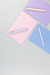 Top view of pink, purple and blue notebooks on grey background. Pink, yellow and blue pens, school, office wallpaper. Flat lay, copy space.