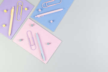 Top view of pink, purple and blue notebooks on grey background. Colorful pens, paperclips, pins, school, office wallpaper. Flat lay, copy space.